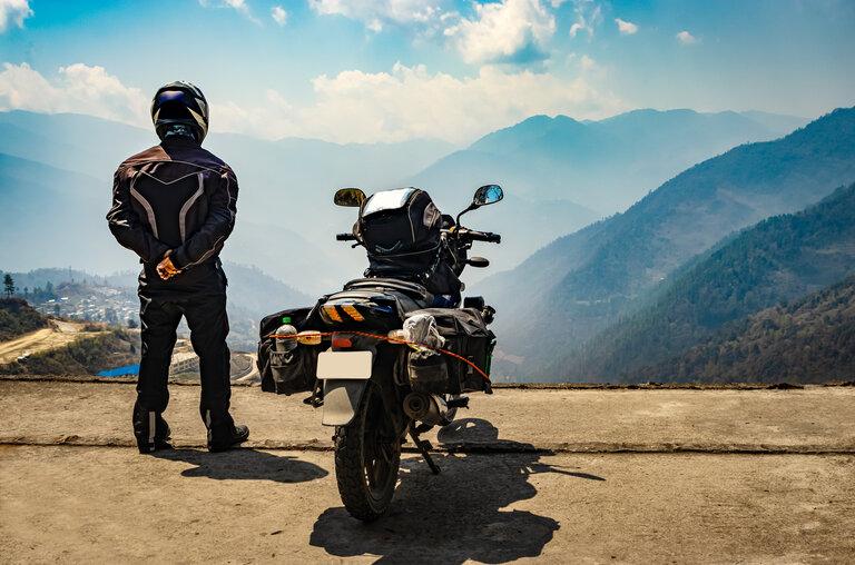Motorradfahrer beobachtet Tal von Hügeln aus, mit seinem beladenen Motorrad neben ihm
