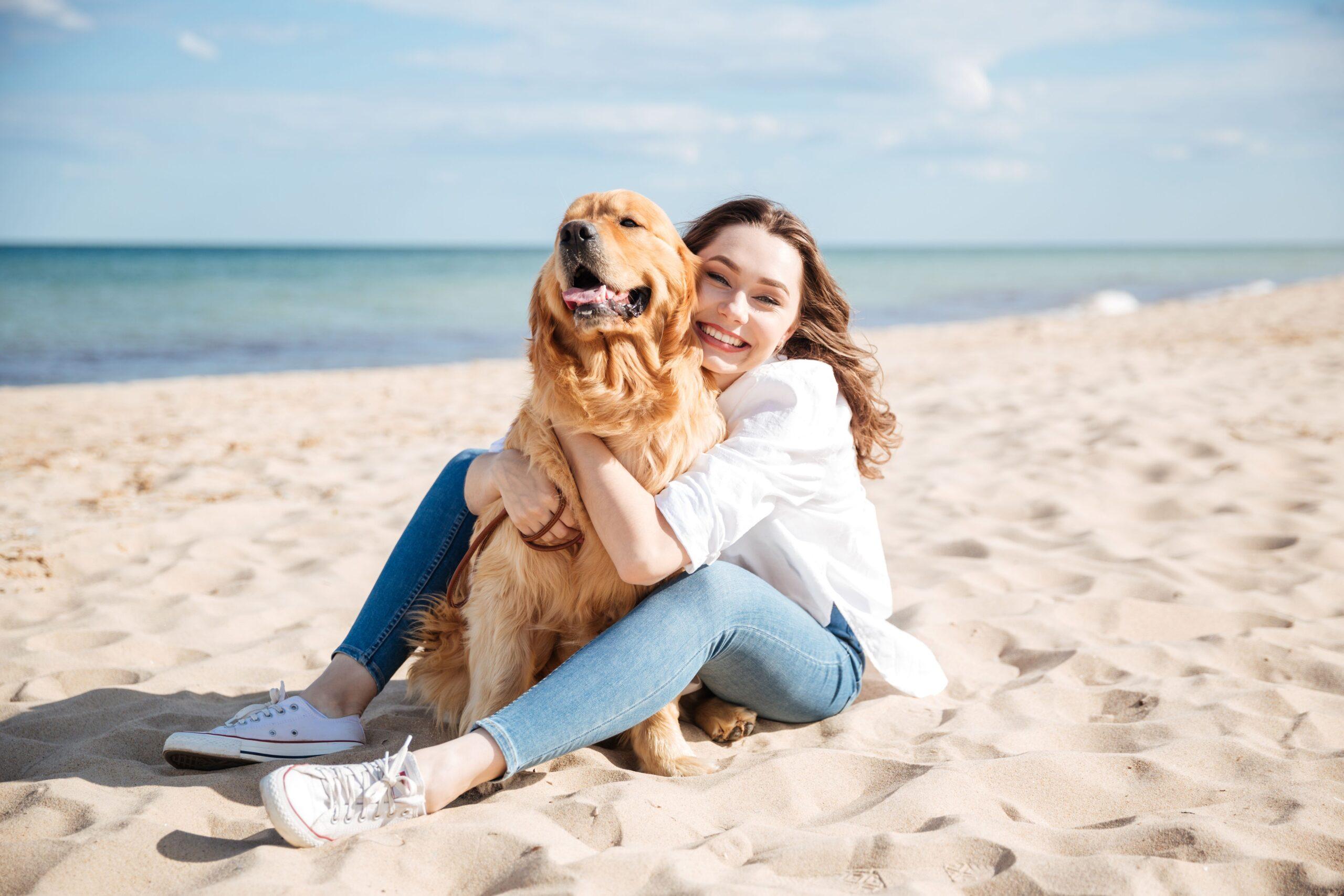 Glückliche Frau sitzt und umarmt ihren Hund am Strand