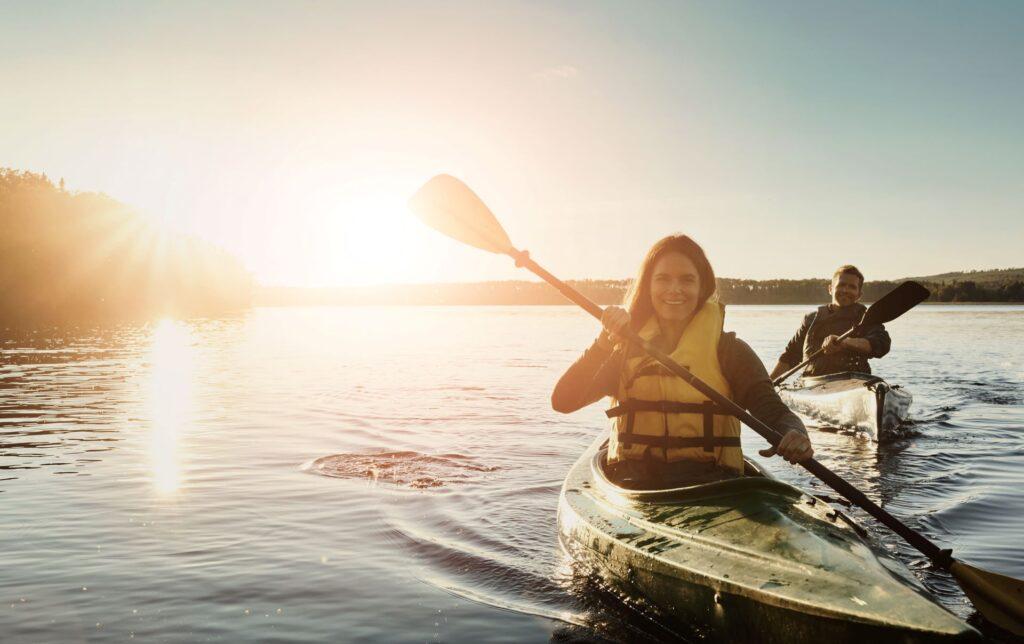 Paar, glücklich und See im Freien für Kajak oder Wassersport in der Natur. Paddeln und Rudern zusammen für eine Flussreise. Mann, Frau und Abenteuerdate zur Bindung mit Liebe, Spaß und Sommerreiseurlaub.