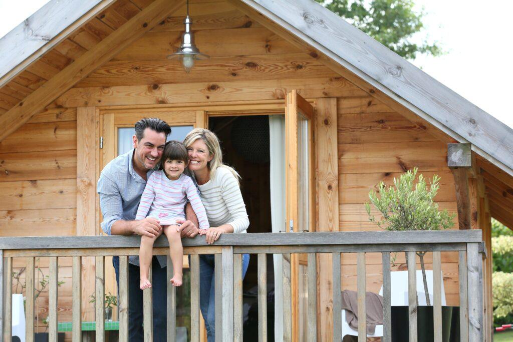 Eine glückliche Familie steht auf der Veranda ihres gemütlichen Holzferienhauses und lächelt in die Kamera