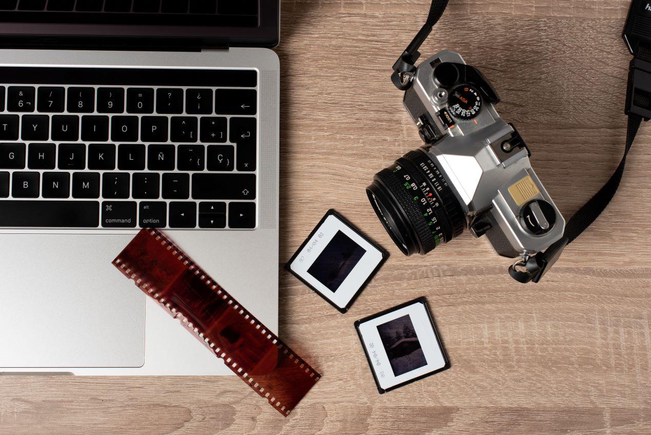 Analoge Kamera, Laptop und Filmstreifen auf einem Holztisch, ideal für den Prozess der Fotos digitalisieren.