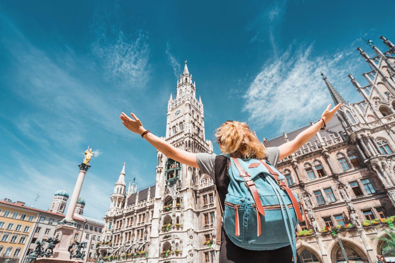 Klassenfahrt München: Schülerin mit Rucksack vor dem Neuen Rathaus am Marienplatz bei blauem Himmel