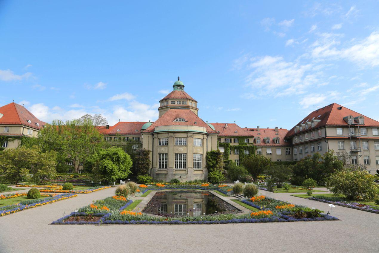 Klassenfahrt München: Blick auf den Botanischen Garten mit Blumenbeeten und historischem Gewächshaus